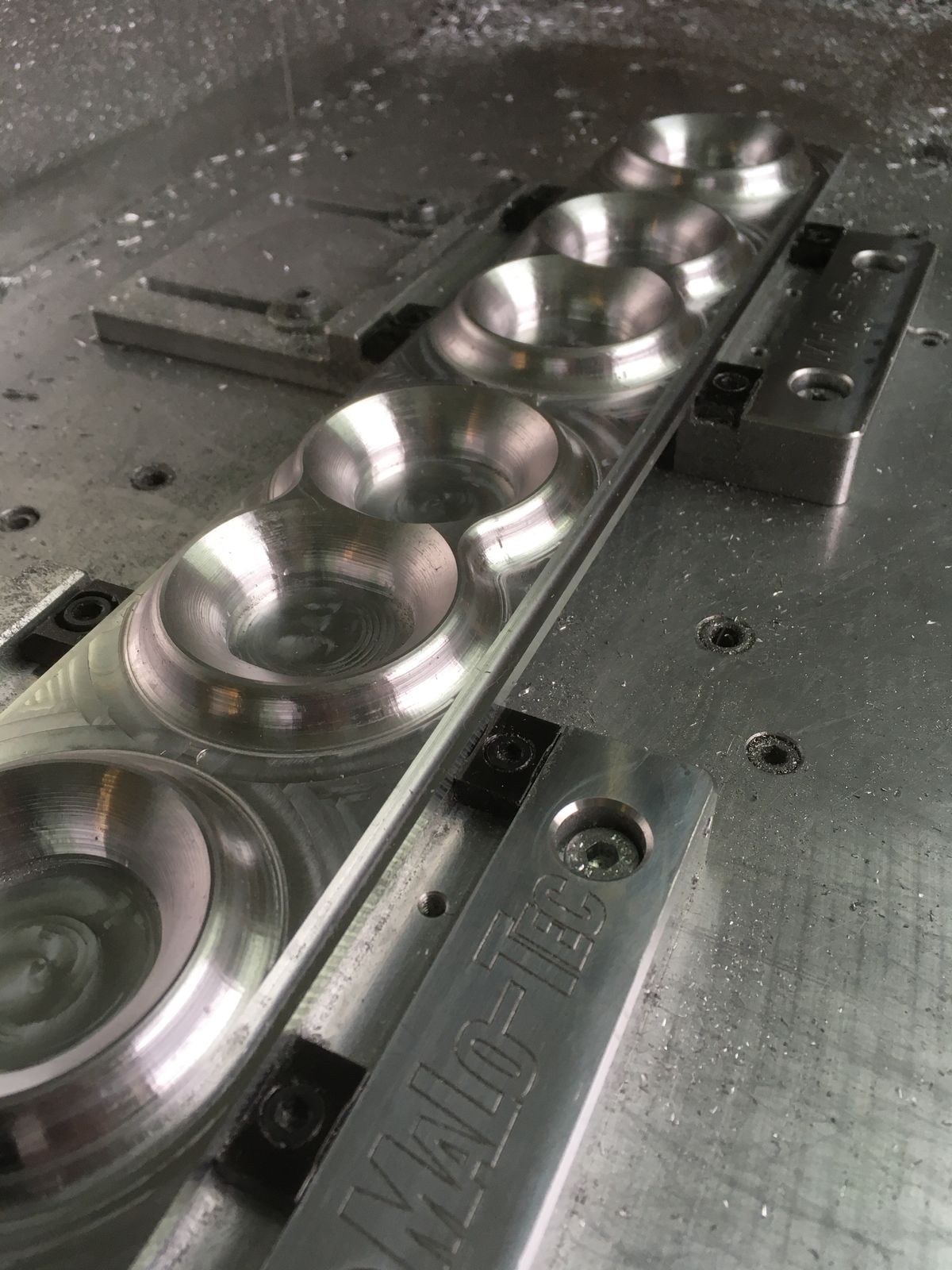 Ein langes Frästeil liegt auf dem Maschinentisch und wird von mehreren Spannblöcken mit MaLo-Tec-Gravur gehalten